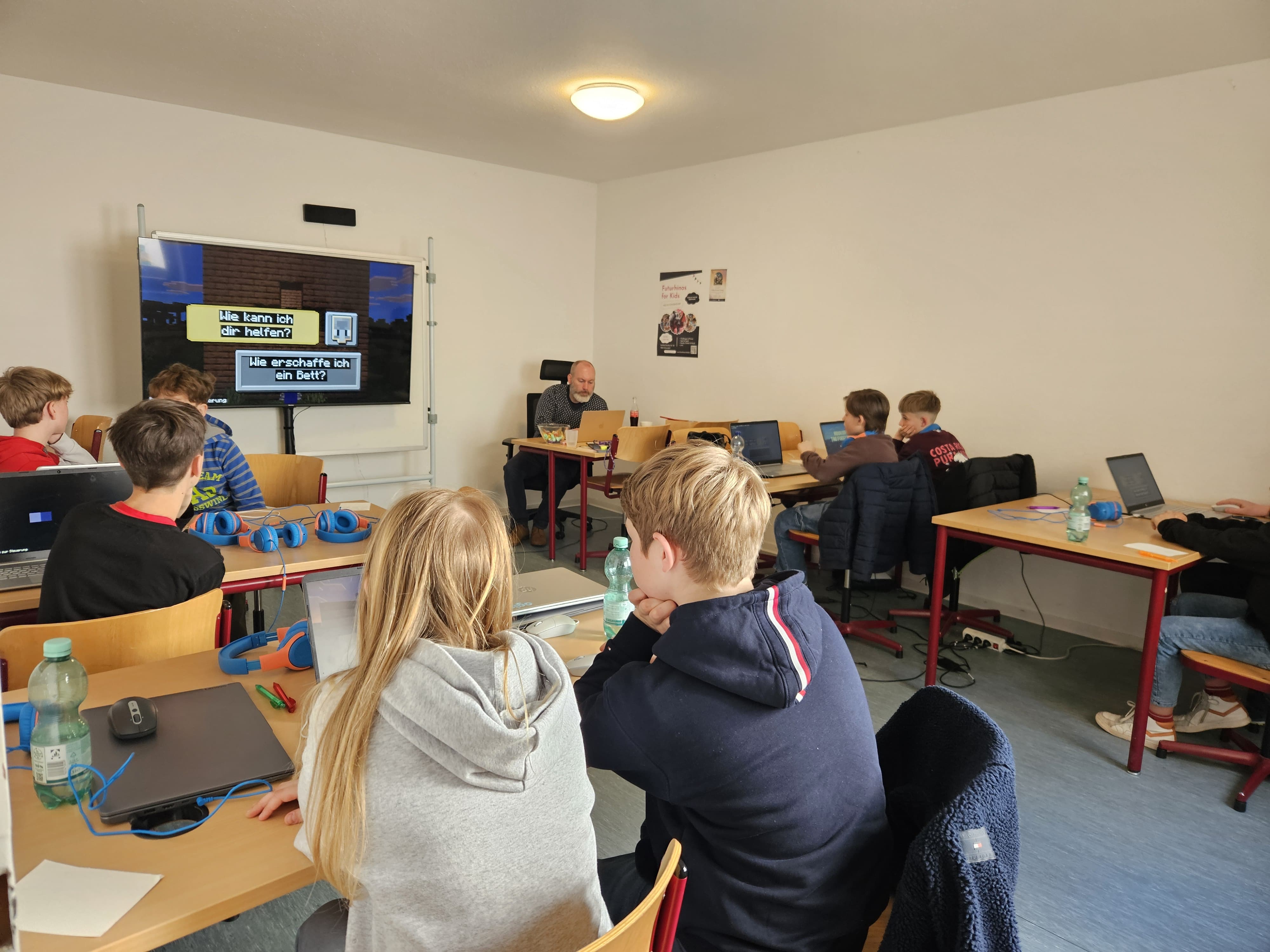 Kinder im Kursraum mit Laptops, René erklärt Minecraft auf großem Bildschirm