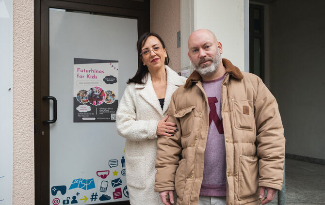 Astrid und René im Eingangsbereich vor der Tür mit Tech-Icons